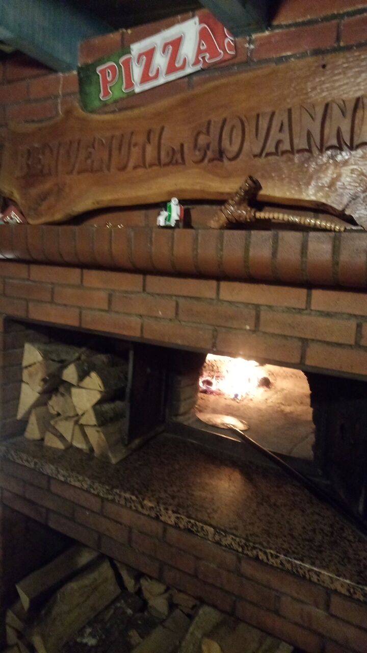 Le four à bois en flammes sous l’enseigne sculptée Benvenuti da Giovanni